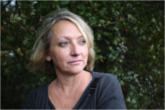 Sarah Pickthall looks to the right of the frame, standing in front of a tree or bush